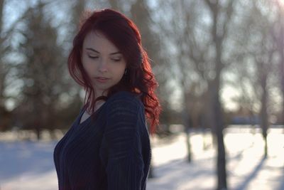 Thoughtful young woman looking away while standing in forest during winter