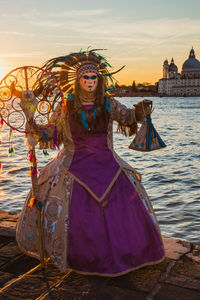 Woman standing at shore against sky during sunset