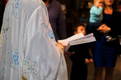 Midsection of priest reading bible by people in church