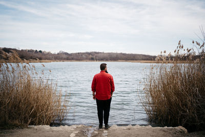 Rear view of man standing on lake against sky