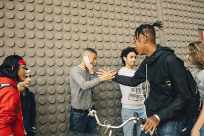 Males shaking hands while standing by friends against wall