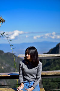 Young woman sitting at observation point against blue sky