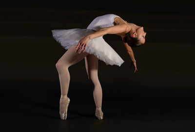 Full length of young woman dancing against black background