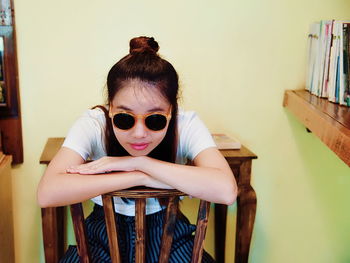 Portrait of woman wearing sunglasses while sitting on chair at home