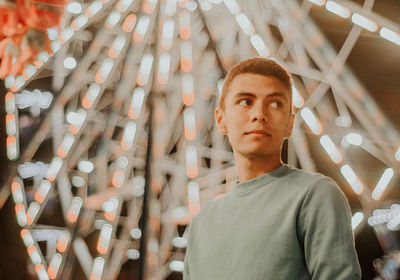 Man looking away while standing against illuminated ferris wheel