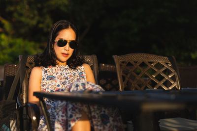 Portrait of young woman wearing sunglasses while sitting at restaurant