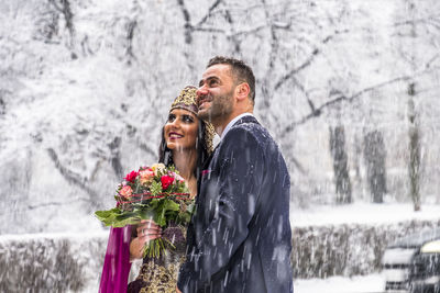 Happy couple standing against snow during winter