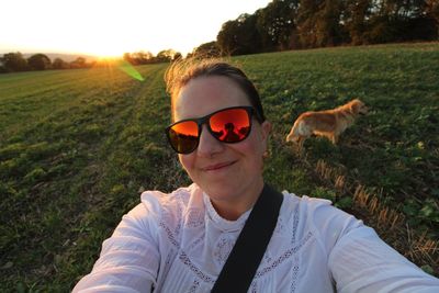 Close-up portrait of woman wearing sunglasses while standing on grassy field during sunset