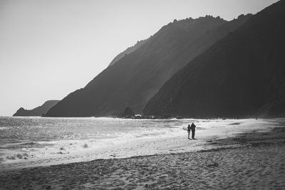 Rear view of man and woman walking at sandy beach