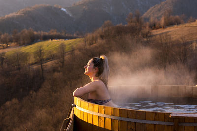 Young woman relaxes in barrel with hot water, at sunset, transyl