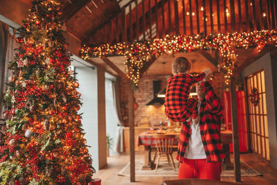 Candid authentic happy dad and son in red plaid pajamas fooling around at wood lodge xmas decorated