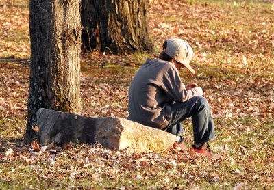 Full length of boy sitting on rock in forest