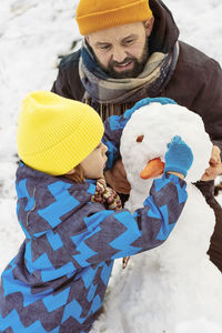 Joyful dad and son enjoying building a snowman.