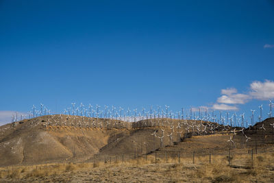 Windmills on mountains at desert against blue sky