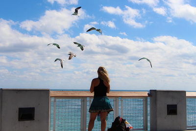 Girl looking at flying birds on miami beach against sky