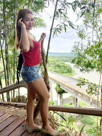 Beautiful woman standing by railing against trees