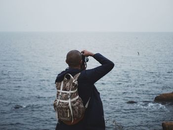 Rear view of man photographing sea through camera against sky