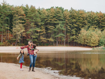 Full length of young woman standing by lake against trees