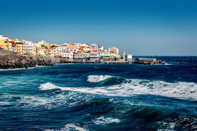 Sea by cityscape against clear blue sky