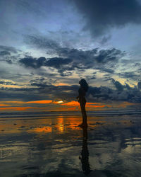 Silhouette woman standing on beach against sky during sunset