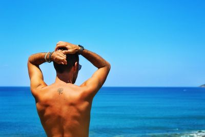 Shirtless man standing at beach against clear blue sky