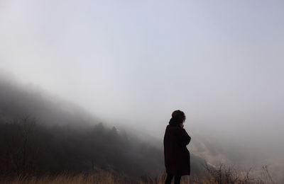 Rear view of man standing on field in foggy weather