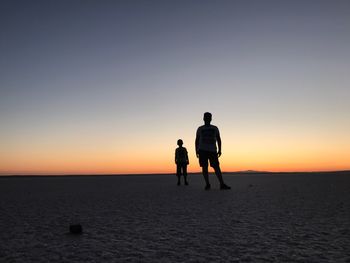 Silhouette people standing at desert against sky during sunset