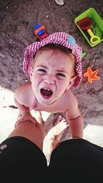 Directly above shot of girl crying while holding father's legs at beach