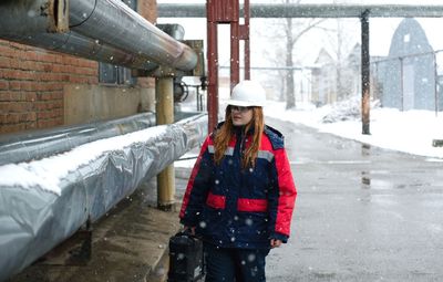 Young woman worker standing in snow in an industrial area