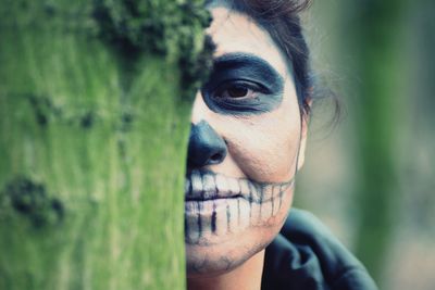 Portrait of woman dressed as zombie by tree trunk