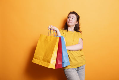 Young woman holding shopping bags against yellow background