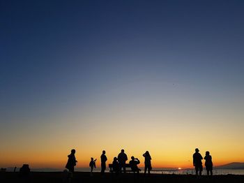 Silhouette people standing on beach against clear sky during sunset