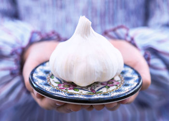 Cropped hand of woman holding garlic in plate