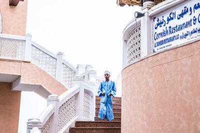 Low angle view of man standing by building against clear sky