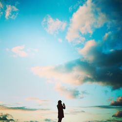 Rear view of silhouette person photographing against cloudy sky during sunset