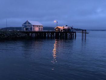 Stilt house by sea against sky at dusk