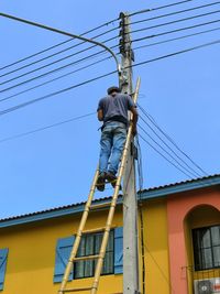 Low angle view of man working against clear blue sky