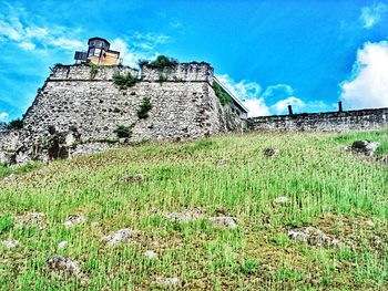 Low angle view of built structure on grassy field against cloudy sky