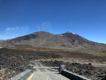 Road leading towards mountains against clear blue sky