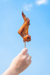 Midsection of person holding ice cream against blue sky