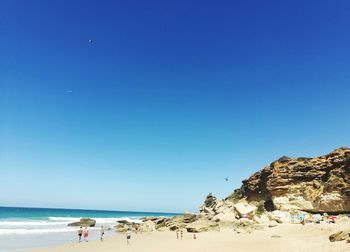 People on beach against clear blue sky