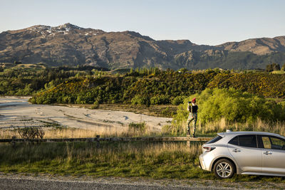 Woman and car overlooking a river and mountain landscape, new zealand