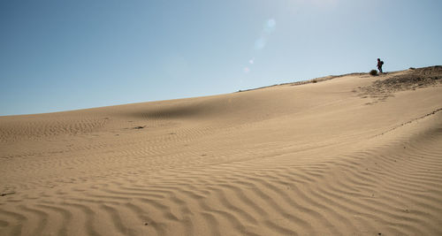 People on sand dune in desert against clear sky