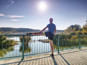 Runner in black leggings makes body stretching on bridge path. fit young man is doing exercise 