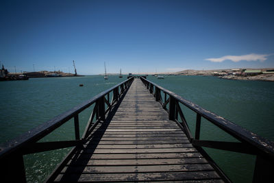 Pier over sea against clear blue sky