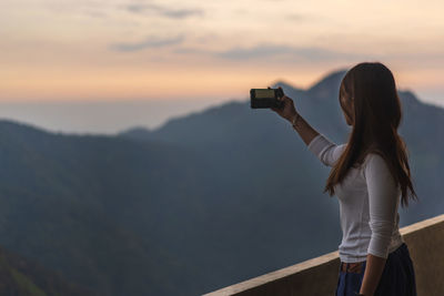 Rear view of woman photographing against sky