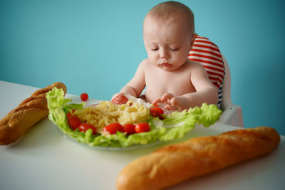 A child eats sausage with pasta and baguette