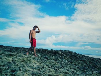 Full length of shirtless man walking on rock against sky