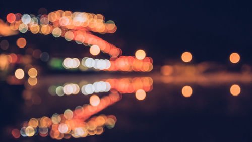 Defocused image of illuminated lights against sky at night