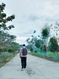 Rear view of man walking on road against sky